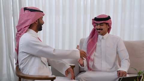 التعاقد مع أطراف متنوعة لتوسيع مجال العمل، مفهوم الإدارة المتعاونة لتحقيق أهداف الشركة، رجلين عربيين خليجيين سعوديين مبتسمين يرتديان الشماغ والثوب التقليدي يتصافحان بإيماءات السرور بنجاح الصفقة، تحقيق مكاسب و أرباح عالية