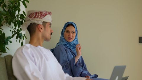 الحوارات والنقاشات ضمن الفريق، مفهوم إدارة شؤون الأعمال وتنظيمها, استخدام الاجهزة و التقنيات الحديثة المتطورة, ايماءات التركيز و الاندماج, رجل اعمال عربي خليجي عماني يرتدي الدشداشة و العمامة يقوم بتوضيح مهام العمل للموظفة عبر جهازالحاسب المحمول