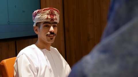 Discussion of work tasks, a close-up shot of an Arab Gulf Omani businessman wearing a dishdasha and a turban sitting in a business meeting at the company's headquarters, following up on work to achieve goals, collaboration among colleagues.
