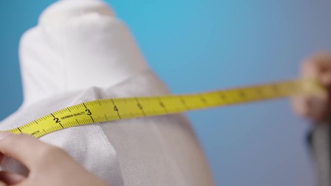 The production of women's clothing with diverse tastes, professions, and works of sewing and design, a close-up portrait of the hand of an Arab Gulf Saudi fashion designer standing in front of a mannequin taking measurements with a measuring tape, colorful background.