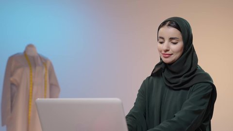 لتدريب من خلال الإنترنت، استخدام التقنيات الحديثة والمتطورة، تصويرلامراة عربية خليجية سعودية ترتدي العباءة السوداء تقوم بالعمل على الحاسب المحمول ، الحصول على المستلزمات اللازمة عن طريق الأونلاين، التسوق عبر المواقع الالكترونية، خلفية ملونه