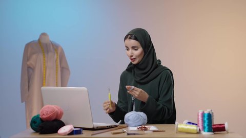 اجراء مكالمة فيديو عبر الحاسب المحمول ، فنون الخياطة و التصميم ، الإبداع في إنتاج موديلات مبتكرة وحديثة، ممارسة مهنة الخياطة، تصويرلامراة عربية خليجية سعودية محجبه ترتدي العباءة السوداء تستخدم إبرة الكروشيه وخيوط الصوف ، أعمال تقليدية شعبية، ايماءات السعادة و السرور