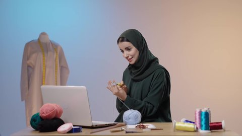 فنون الخياطة و التصميم ، الإبداع في إنتاج موديلات مبتكرة وحديثة، ممارسة مهنة الخياطة، تصويرلامراة عربية خليجية سعودية محجبة ترتدي العباءه السوداء تستخدم إبرة الكروشيه وخيوط الصوف تجلس امام الحاسب المحمول ، أعمال تقليدية شعبية، ايماءات السعادة و السرور