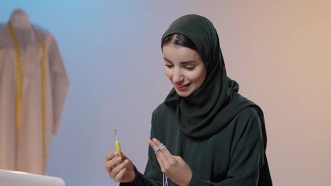 ابتكار موديلات عصرية بإبداع ، ممارسة مهنة الخياطة، تصوير مقرب لامراة عربية خليجية سعودية ترتدي العباءة السوداء تستخدم إبرة الكروشيه وخيوط الصوف تجلس امام الحاسب المحمول ، أعمال تقليدية شعبية, فنون الخياطة و التصميم ، ايماءات السعادة و السرور