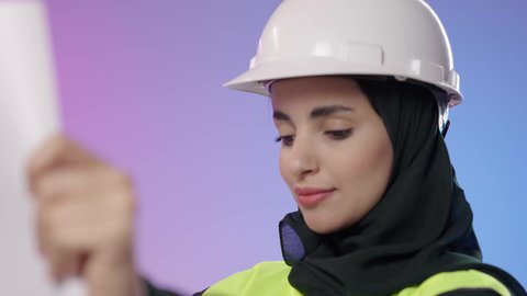 متابعة سير العمل بالمشاريع الهندسية, المخططات الانشائية المعمارية, تنمية وتطور السعودية على يد أبناء الوطن, بورترية مقرب لمهندسة عربية خليجية سعودية مبتسمة ترتدي الخوذة وسترة الحماية تمسك بيدها المخطط تنظر إلى شي ما