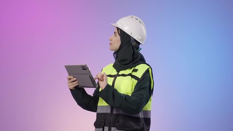 المخططات و التصماميم الهندسية الالكترونية، دمج البيئة العملية و الهندسه مع التقنية و التكنولوجيا, بورتريه لامراة عربيه خليجيه سعودية محجبه ترتدي الخوذة وسترة الحماية تحمل بيديها جهاز التابلت و تقوم بالنظر الى شيء ما، خلفية ملونه