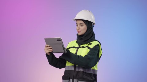 دمج البيئة العملية و الهندسه مع التقنية و التكنولوجيا، المخططات و التصماميم الهندسية الالكترونية, بورتريه لامراة عربيه خليجيه سعودية محجبه ترتدي الخوذة وسترة الحماية تحمل بيديها جهاز التابلت و تقوم بالنظر الى شيء ما، خلفية ملونه