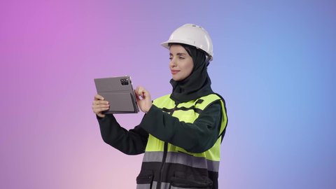 المخططات و التصماميم الهندسية الالكترونية، دمج البيئة العملية و الهندسه مع التقنية و التكنولوجيا, بورتريه لامراة عربيه خليجيه سعودية محجبه ترتدي الخوذة وسترة الحماية تحمل بيديها جهاز التابلت و تقوم بالنظر الى شيء ما، خلفية ملونه