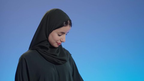 التسوق في المراكز التجاريه، بورتريه مقرب لإمرأة عربيه خليجية سعوديه محجبة ترتدي عباءه سوداء تحمل بيدها أكياس التسوق, الاستمتاع بالتبضع فى السعودية, عروض وتخفيضات موسميه, إيماءات تدل على السعاده، خلفية ملونه