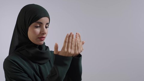 الإجتهاد في العبادة والحفاظ على الصلوات، ايماءات تدل على التوسل والتضرع، الدعاء والطلب والتمني من الله، بورتريه مقرب لامراة عربية سعودية خليجية ترتدي الحجاب والعباءة السوداء  ترفع يديها وتدعو الله، خلفية ملونه