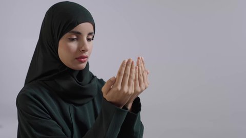 تعابير تدل على التوسل والتضرع، أداء الفروض على وقتها, التقرب الى الله من خلال الإجتهاد في العبادة والحفاظ على الصلوات، بورتريه مقرب لإمرأة عربية سعودية خليجية ترتدي الحجاب والعباءة ألسوداء  ترفع يديها وتدعو الله