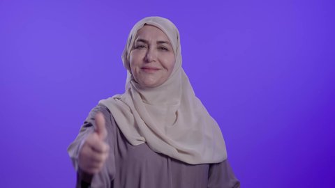 تعابير الرضا والإعجاب, النظر إلى الكاميرا بإيماءات السعادة والسرور, علامة الجودة والامتياز, مفهوم الموافقة والقبول, تصوير لامراه عربيه خليجيه سعوديه كبيره بالسن ترتدي العباءة والحجاب تشير بإصبع الإبهام للأعلى