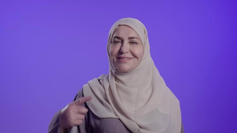 تجنب التسوس وأمراض اللثة, العناية والاهتمام بصحة ونظافة الفم،مفهوم تبييض وتجميل ومعالجة الأسنان، تصوير لامراه عربيه خليجيه سعوديه كبيره بالسن ترتدي العباءة والحجاب تشير بإصبع السبابة إلى أسنانها