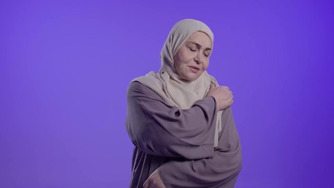 الإحساس بوجع في عضلات الكتف، الحاجة للعلاج والذهاب للطبيب, التألم والشعور بالتعب والإرهاق, آلام العظام والمفاصل,تصوير لامراه عربيه خليجيه سعوديه كبيره بالسن ترتدي العباءه والحجاب تضع يديها على كتفها بتعابير الألم