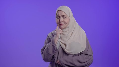الحاجة للعلاج والذهاب للعيادة السنية, التألم والشعور بالتعب والمرض, الإحساس بوجع الأسنان والنخور،  تصوير لامراه عربيه خليجيه سعوديه كبيره بالسن ترتدي العباءه والحجاب تضع يدها على خدها بتعابير الألم