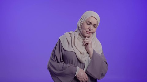 الإحساس بوجع الأسنان والنخور، الحاجة للعلاج والذهاب للعيادة السنية, التألم والشعور بالتعب والمرض,  تصوير لامراه عربيه خليجيه سعوديه كبيره بالسن ترتدي العباءه والحجاب تضع يدها على خدها بتعابير الألم