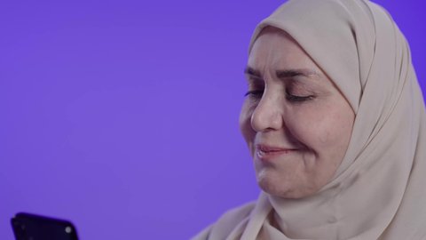 تصفح مواقع وتطبيقات الانترنت، النظر إلى الهاتف المحمول بإيماءات الاندماج، الدردشة والتحدث مع الأصدقاء،  تصوير لامراه عربيه خليجيه سعوديه كبيره بالسن ترتدي العباءه والحجاب تمسك الجوال بيدها، استخدام التقنيات والتكنولوجيا الحديثة بالحياة اليومية