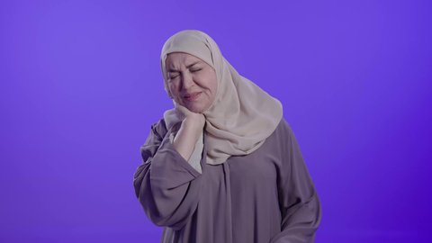 آلام العظام والمفاصل, التألم والشعور بالتعب والإرهاق,  الحاجة للعلاج والذهاب للطبيب,  الإحساس بوجع في الرقبة،تصوير لامراه عربيه خليجيه سعوديه كبيره بالسن ترتدي العباءه والحجاب تضع يديها على عنقها بتعابير الألم