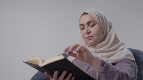 ممارسه الهوايات المفضله، قضاء وقت الفراغ بالتثقيف والتعلم، القراءه بإيماءات التمعن والتركيز ،تصوير لامراه عربيه خليجيه سعوديه كبيره بالسن ترتدي العباءه والحجاب تجلس على كرسي ،تمارس هواية مطالعة الكتب المفيدة في وقت الفراغ، مفهوم محو الأمية، التزود بالعلم والمعرفة