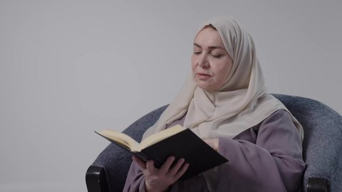 قضاء وقت الفراغ بالتثقيف والتعلم، التزود بالعلم والمعرفة،مفهوم محو الأمية، تصوير مقرب لامراه عربيه خليجيه سعوديه كبيره بالسن ترتدي العباءه والحجاب تجلس على كرسي، تمارس هواية مطالعة الكتب المفيدة في وقت الفراغ، القراءه بإيماءات التمعن والتركيز