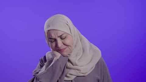 التألم والشعور بالتعب والإرهاق,  الحاجة للعلاج والذهاب للطبيب,  الإحساس بوجع في الرقبة،آلام العظام والمفاصل, تصوير لامراه عربيه خليجيه سعوديه كبيره بالسن ترتدي العباءه والحجاب تضع يديها على عنقها بتعابير الألم