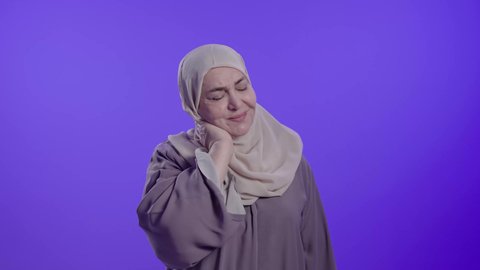 التألم والشعور بالتعب والإرهاق,  الحاجة للعلاج والذهاب للطبيب,  الإحساس بوجع في الرقبة،آلام العظام والمفاصل, تصوير لامراه عربيه خليجيه سعوديه كبيره بالسن ترتدي العباءه والحجاب تضع يديها على عنقها بتعابير الألم