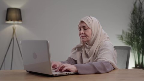 تصفح برامج التواصل الاجتماعي, تطور التكنولوجيا والأجهزة التقنية، ادارة الأعمال عن بعد، تصوير لامراه عربيه خليجيه سعوديه كبيره بالسن ترتدي العباءه والحجاب تجلس على مكتب وتعمل على جهاز الحاسب المحمول ،استخدم التقنيات الحديثة في الأعمال الإدارية ،التوظيف في المكاتب والشركات ،  التركيز والتفاني والعمل الجاد