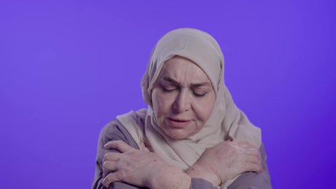 تصوير مقرب لامراه عربيه خليجيه سعوديه كبيره بالسن ترتدي العباءه والحجاب تقف بجركات يد وإيماءات الشعور بالصقيع والقشعريرة والتجمد، الإحساس الشديد بالبرد في الأجواء الشتوية