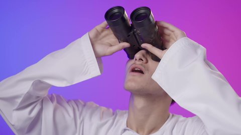 إيماءات الذهول والتفاجؤ, حب الاستكشاف و المغامرة, بورتريه مقرب لولد عربي خليجي عماني يرتدي الدشداشة و الكمة يحمل بيده منظار ثنائي العينين ينظر إلى شيئ ما, مفهوم النظرة المستقبلية، رؤية الاشياء البعيدة عبر التلسكوب، خلفية ملونه