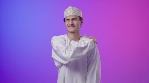 الإحساس بالتعب والإرهاق، التهاب العضلات والمفاصل، شد عضلي في الرقبه، الحاجه للراحة و وضع خطة علاجية , بورتريه لولد  عربي خليجي عماني يرتدي الدشداشة و الكمة يضع يده على رقبته بإيماءات الألم، خلفية ملونه
