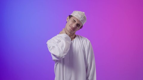 شد عضلي في الرقبه، الحاجه للراحة و وضع خطة علاجية ،التهاب العضلات والمفاصل، الإحساس بالتعب والإرهاق, بورتريه لولد  عربي خليجي عماني يرتدي الدشداشة و الكمة يضع يده على رقبته بإيماءات الألم، خلفية ملونه