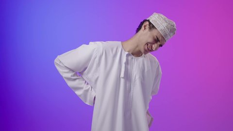 التهاب العضلات والمفاصل، الأوجاع والآلام العصبية، طلب المساعده والحاجه للعلاج، بورتريه لولد عربي خليجي عماني يرتدي الدشداشة و الكمه يضع يده على ظهره بايماءات الألم والتعب والأرهاق، خلفية ملونه
