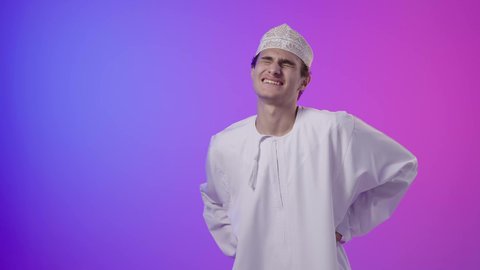 طلب المساعده والحاجه للعلاج، الأوجاع والآلام العصبية، التهاب العضلات والمفاصل، بورتريه لولد عربي خليجي عماني يرتدي الدشداشة و الكمه يضع يده على ظهره بايماءات الألم والتعب والأرهاق، خلفية ملونه