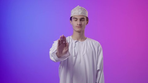 إيماءات يدين تدل على الأمر بالتوقف عن فعل شيء ما و النهي عنه, بورترية لولد عربي خليجي عماني يرتدي الدشداشة و الكمة  يرفع كفه للاعلى ويشعر بالإنزعاج و الرفض والإمتناع، خلفية ملونه