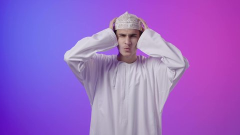 الاحساس بالشقيقية والصداع النصفي,، الشعور بالإرهاق وفقدان التركيز، الاجهاد والضغط النفسي, بورتريه لولد عربي خليجي عماني يرتدي الدشداشة و الكمه يضع يديه على رأسه ويغمض عينيه بإيماءات ألم الرأس الشديد, خلفية ملونه