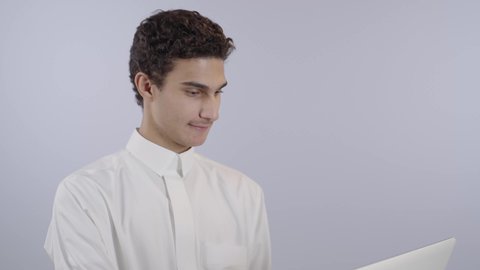 ايماءات الاندماج و التركيز، حل الواجبات المنزليه عبر اللابتوب، ادخال التقنية والتكنولوجيا بالتعليم، بورتريه مقرب لولد عربي خليجي سعودي يرتدي الثوب الابيض يقوم بمتابعة منصات التعليم الالكتروني المتاحة عبر الانترنت بإستخدام جهاز الحاسب المحمول، خلفية بيضاء