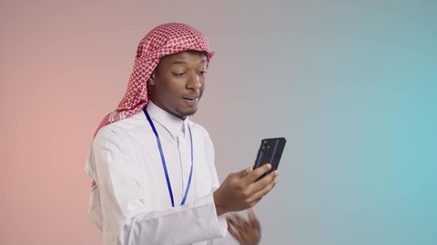 التواصل الفعال عبر الانترنت, شاب عربي خليجي سعودي يرتدي الثوب والشماغ التقليدي يقوم بالتحدث مع شخص ما, استخدام الاجهزه الحديثه, خلفيه ملونه