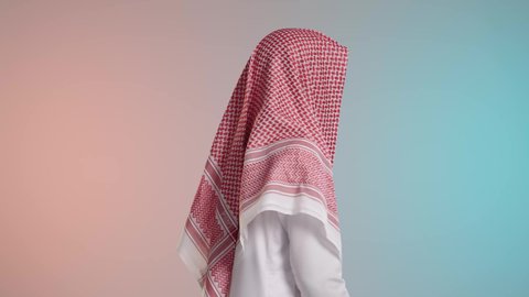 A portrait of a young, dark-skinned Arab Gulf Saudi man smiling, wearing traditional thobe and shemagh, looking confidently and proudly at the camera, with elegance and masculine features, against a colorful background.