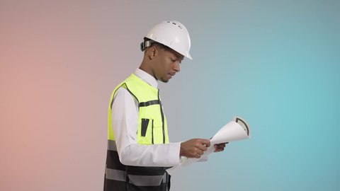 التصاميم المعمارية وتدقيق المخططات, دور الهندسة الإنشائية في تطور المجتمع السعودي, بورتريه مقرب لمهندس عربي خليجي سعودي يرتدي سترة الحماية والخوذة ينظر إلى مخطط الإعمار بإيماءات الفخر, مهن ووظائف هندسيه