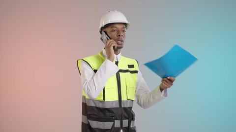 Supervision and control of engineering projects, a portrait of an Arab Saudi Gulf engineer wearing a helmet and safety vest holding a blue file while making a phone call to follow up on work, in the field of construction and engineering projects, colorful background.