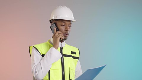 مجال الانشاءات والمشاريع الهندسية, الاشراف والرقابة على المشاريع الهندسية، بورتريه لمهندس عربي سعودي خليجي يرتدي الخوذة وسترة الحماية يمسك بملف ازرق يجري مكالمه هاتفيه لمتابعه العمل، خلفيه ملونه
