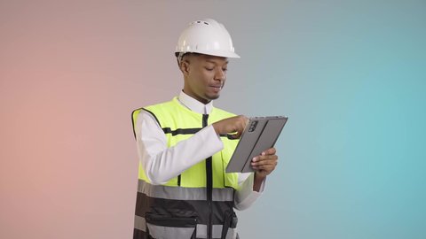 استخدام جهاز تقني حديث متطور في مجال الهندسة، العمل في القطاع الهندسي السعودي، مفهوم ادارة المشاريع الهندسية والانشاءات، مهنة ووظيفة شبابية، بورتريه لمهندس عربي خليجي سعودي يرتدي الثوب التقليدي والسترة وخوذة الحماية يعمل على جهاز التابلت، خلفيه ملونه