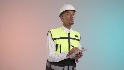 مهن و وظائف هندسية في المملكة العربية السعودية، ادارة المشاريع الهندسية، مفهوم الهندسة الصناعية، الاشراف في موقع العمل، مهندس عربي خليجي سعودي يرتدي خوذة وسترة الحماية خاصة بالعمل يقوم بكتابة وتدوين الملاحظات, خلفيه ملونه