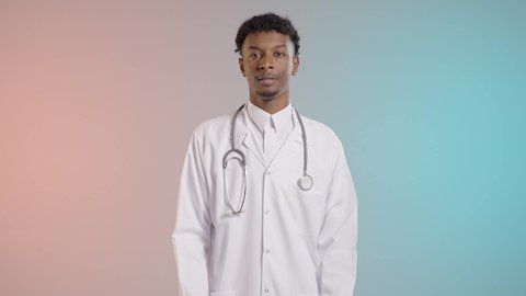 العمل في القطاع السعودي الصحي, طبيب عربي خليجي سعودي مبتسم يرتدي المعطف الأبيض والثوب ويضع سماعة الفحص يقف باستقامة في المستشفي بإيماءات أيدي متقاطعة, النظر إلى الكاميرا بتعابير الثقة بالنفس, خلفيه ملونه