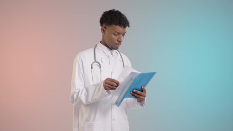 سجل تقارير المرضي باللون الازرق, طبيب عربي خليجي سعودي يرتدي المعطف الابيض والسماعه الطبيه يقوم بفحص النتائج, خلفيه ملونه