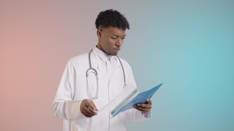 مراجعه التقارير الطبيه, طبيب عربي خليجي سعودي يرتدي معطف وسماعه طبيه يقوم بمراجعه النتائج الخاصه بالمرضي, خلفيه ملونه
