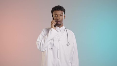 Making a call via mobile phone, an Arab Gulf Saudi doctor wearing a coat and stethoscope is having a phone conversation, colorful background.