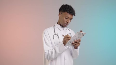 طبيب عربي خليجي سعودي يرتدي المعطف والسماعه الطبيه يقوم بكتابه التقارير الطبيه في السجل الطبي, التطور الطبي في المملكه العربيه السعوديه, خلفيه ملونه