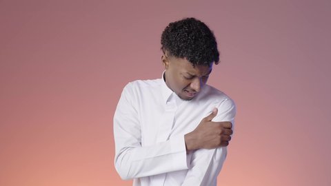 الإحساس بالمرض ووجع العظام والعضلات، طلب المساعده والحاجه للعلاج، الأوجاع والآلام العصبية والعضلية، شاب عربي خليجي سعودي يرتدي الثوب التقليدي يمسك بكتفه من شده الالم, الانزعاج من الم المفاصل, خلفيه ملونه