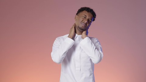 Symptoms of insomnia and feeling pain in the neck and joints, a young Arab Gulf Saudi man wearing traditional attire feels extremely fatigued and places his hand on his neck, colorful background.